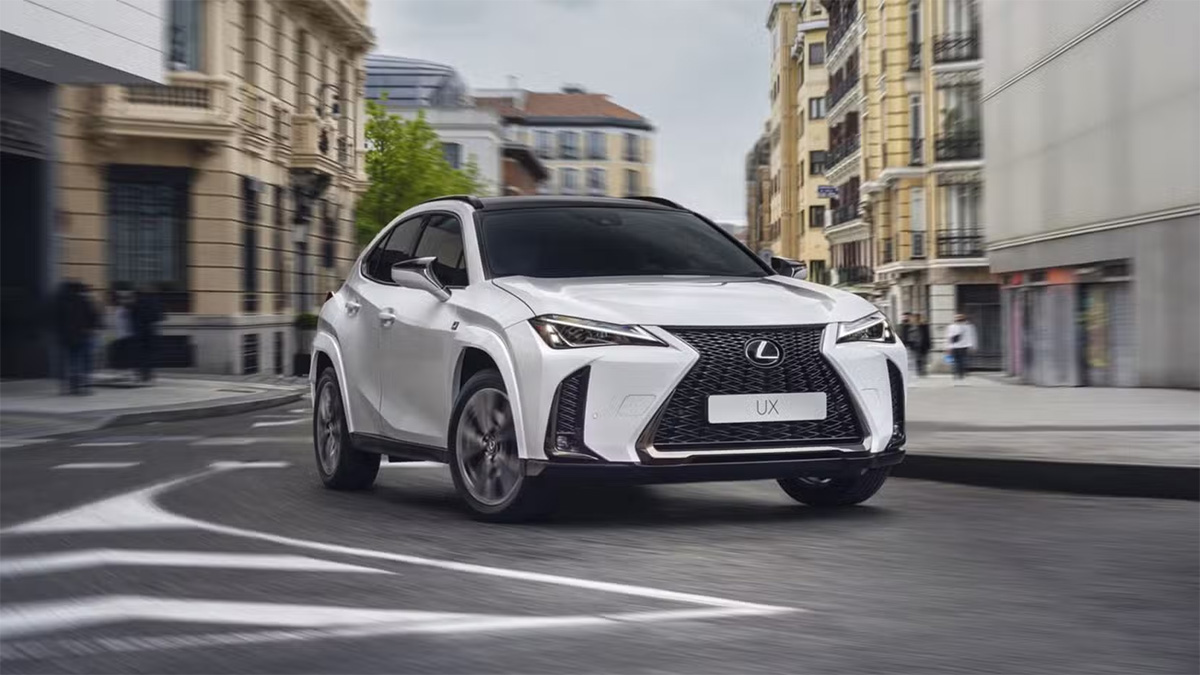 Lexus UX blanc roulant dans une rue urbaine avec immeubles en arrière-plan