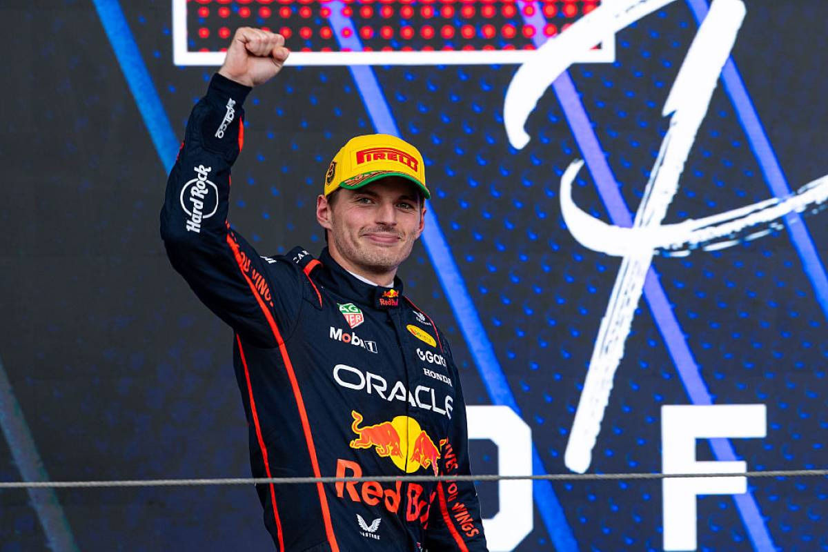 Max Verstappen lève le poing sur le podium en tenue Red Bull, casque retiré et casquette Pirelli